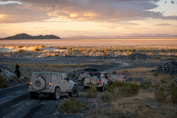 Jeeps parked on a slope overlooking a barren desert with mountains in the distance.