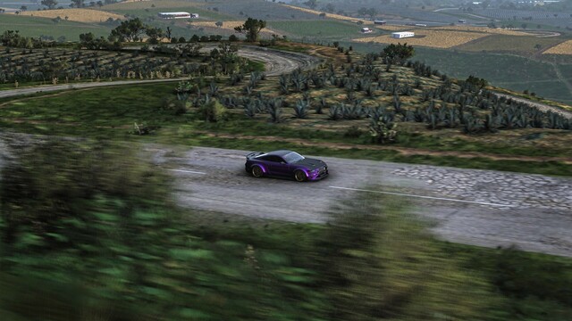 Distance capture of a purple 2018 Ford Mustang RTR Spec 5 on a hilly road in Mexico with agave plants and agricultural fields covering the hills in the distance.