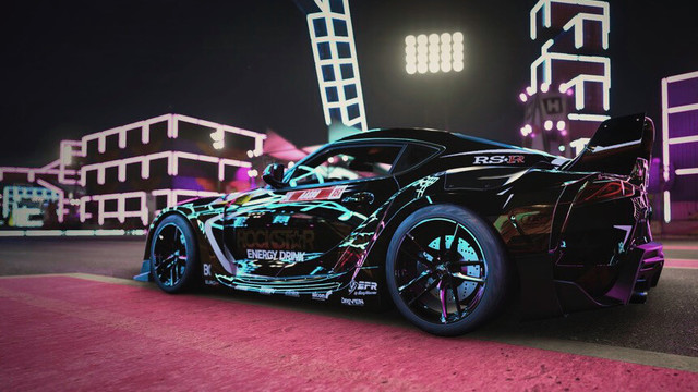 Close up shot of the driver side of a black and gold 2020 Toyota GR Supra reflecting magenta, cyan, and yellow neon slights. Neon structures and stadium lightly are softly blurred in the distance.
