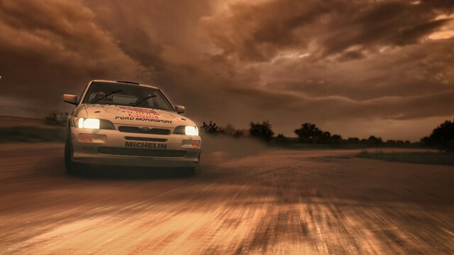 Close-up taken from the front of a 1992 Escort RS Cosworth in a retro green, gray, and white Fujifilm livery as it drifts at full wheel lock around a dirt corner. Ominous clouds fill the sky and mingle with the dust. The sunset casts a golden glow on everything.