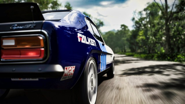 Close-up shot of 1973 Ford Capri RS3100 taken from the rear passenger side. The road and trees blur with speed as the sun reflects off the dark blue and white livery.