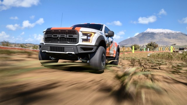 Close up of the front of a 2017 Ford F-150 Raptor with a silver, black, and orange striped livery  cresting a hill. The suspension is lifting as the gravity shifts.