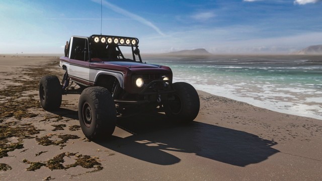 2017 Ford #25 â€œBrockyâ€� Ultra4 Bronco RTR with large offroad tire, lifted suspension, a full roll cage, light bars, and a large spare strapped to the back on the beach. The body is painted in brick red with a large white cutout and black pin striping. Seaweed is scattered to one side while wave lap in on the other.