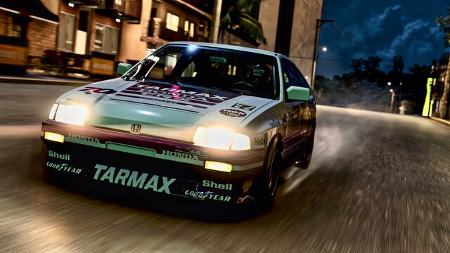 Close up from the front of a 1984 Honda CRX Mugen edition in a retro Tarmax livery driving on wet asphalt through a well lit city. Storm clouds loom behind and the tires kick up streams of water.