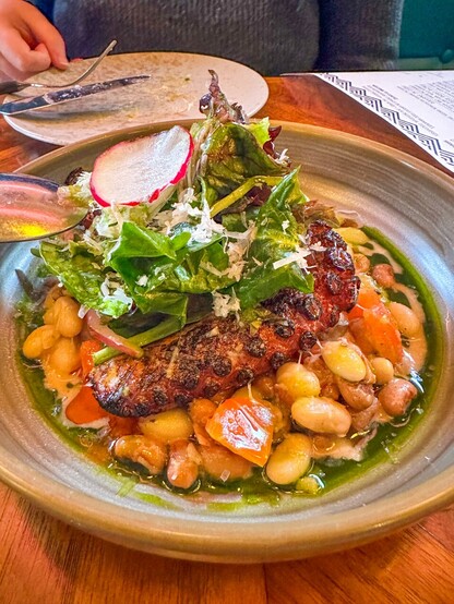 A charred octopus dish served with greens and beans