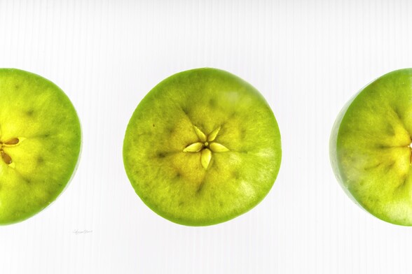 Three green apple slices. The center slice stands on its own. The center of the slice is a star. The other apples sit on either side and are cut off by the edge of the frame.