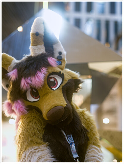 A brown dog fursuiter, with pink air highlights. Her eyes have small hearts in them, and she is looking adorably