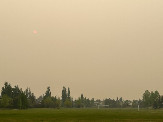 smoke filled skies over a suburban Edmonton park with a eerie red dot of the sun mid way into the sky