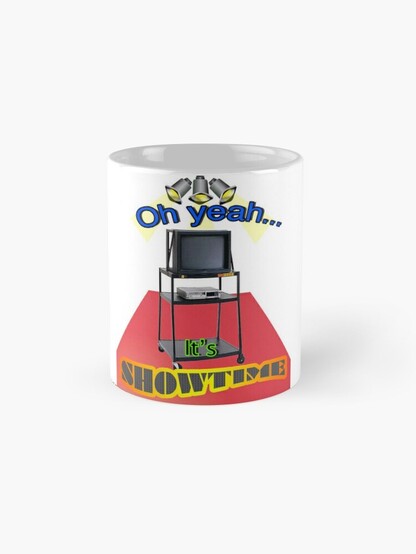 A white mug with the graphic shown on the front. The graphic has the words. Oh yeah, itâ€™s showtime and the image on the graphic is of three spotlights shining down on a cathode ray television set which is placed on top of a metal rolling media cart on top of a red carpet