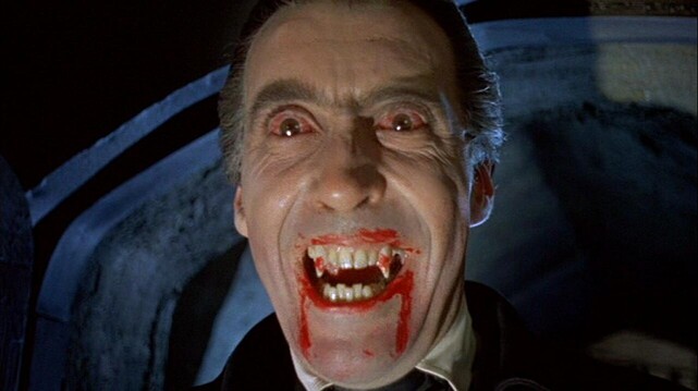 Christopher Lee as Dracula with a pair of bloodied fangs and two crimson streaking his chin.