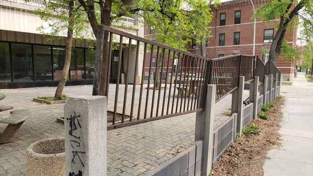 Concrete posts and lower halfs that make up a wall around the front of an apartment building, with slats of iron fence pulled up to different heights usually uneven.