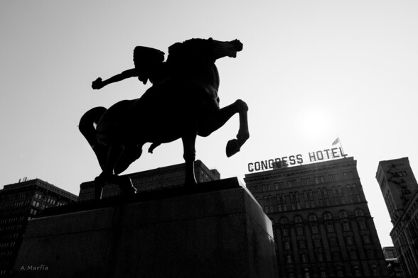 A black and white photograph in Chicago of the Spearman sculpture in Grant Park. Visible beyond the statue is the Congress Hotel sign on Michigan Avenue.