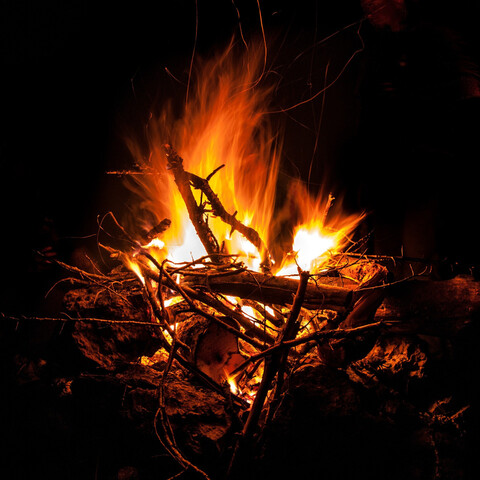 Big fire with gold and orange flames, made mostly of lots of small branches and twigs. Black background. Image: Jordy on Pixabay.