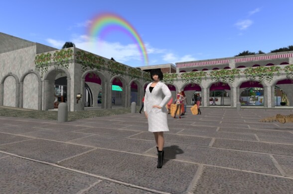 Me standing at the harbour at Simus, wearing a white suit jacket, a black velvet top, a knee-long white skirt, a pair of black stockings and a pair of black ankle boots; in the background, there are Italian-style archways with various shops, a group of static people that serve as teleporters and a rainbow in the sky