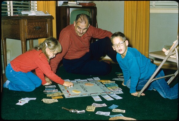 A man and two children sit on a living room floor playing Monopoly.