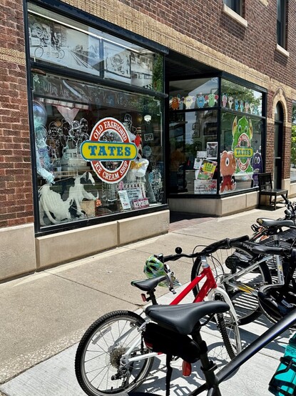 Photo of a store window with the words “Rate’s Old Fashioned Ice Cream Shop”. Multiple bikes are parked in the foreground.