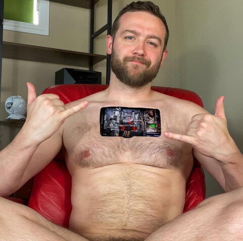 A bearded gay otter sits in a chair with its chest panel open, smiling at you as though he wants you to make some adjustments to his programming and systems