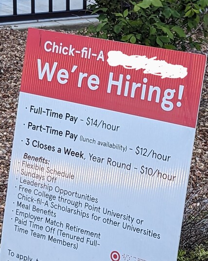 A Chick-fil-A ''now hiring'' sign that is listing pay between $10.00 to $14.00 an hour.