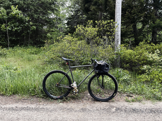 A simple gray bicycle standing at the side of a gravel road.