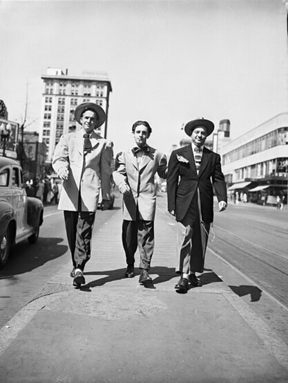 This photograph of three men sporting variations on the zoot suit was taken by Oliver F. Atkins. Atkins worked for the Saturday Evening Post and was a personal photographer to President Richard Nixon. By This photograph of three men sporting variations on the zoot suit was taken by Ollie Atkins. Atkins worked for the ‘Saturday Evening Post’ and was a personal photographer to President Richard Nixon.National Archives, Richard Nixon Library and Museum - http://recordsofrights.org/records/62/zoot-suiters-on-paradehttp://recordsofrights.org/assets/record/000/000/249/249_original.jpg, Public Domain, https://commons.wikimedia.org/w/index.php?curid=63313420