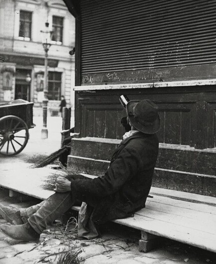 A drunk sitting on a street corner drinking from a bottle. 📸 Emil Mayer