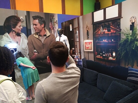 People at the exhibit. At right, a recreation of part of Will and Grace's living room. In front of us, a mannequin with one of Will's costumes, and a wall size photo of the title characters.