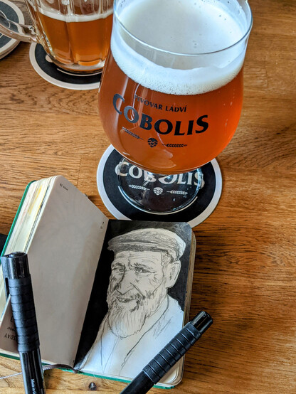 A glass of beer and a sketchbook with a portrait drawing of a man.