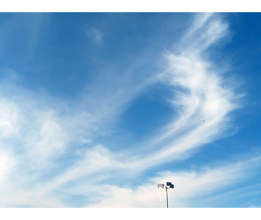 wide shot of a blue morning sky with wispy cloud formations. the tip of an industrial lamppost pushes into the mid-bottom of the picture and is dwarfed by the sky.