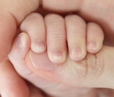 photograph of a baby's hand holding on an adult's hand by the thumb