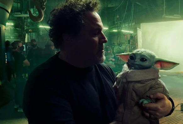 Jon Favreau behind the scenes on the set of The Mandalorian, holding and gazing at Grogu (Baby Yoda).