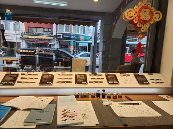 a desk facing out on a street in Taipei, with a display of wooden fountain pens and some small jars of ink laid out alongside paper covered in colourful squiggles