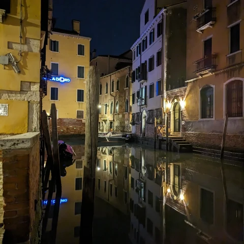 A Venice 'street' photographed at night. Old buildings are reflected in the almost still water.