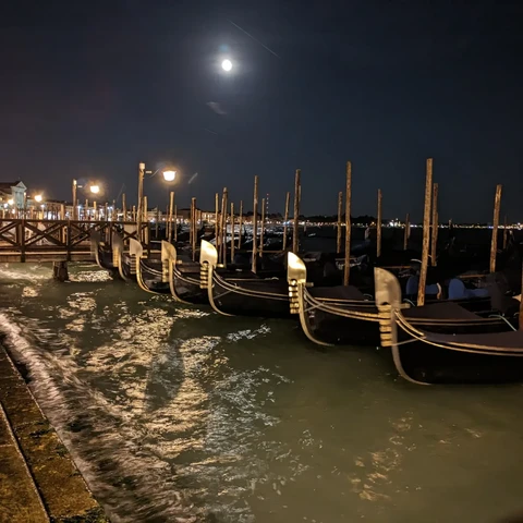 Venetian gondolas, moored in a row. The moon shines upon the dock.