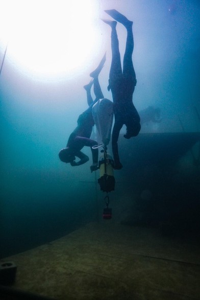 Two freedivers diving onto an underwater platform in a lake using a weighted sled