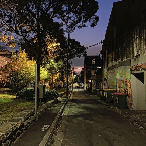Laneway in Redfern at dusk. Street lights light up a small park to the left of the lane