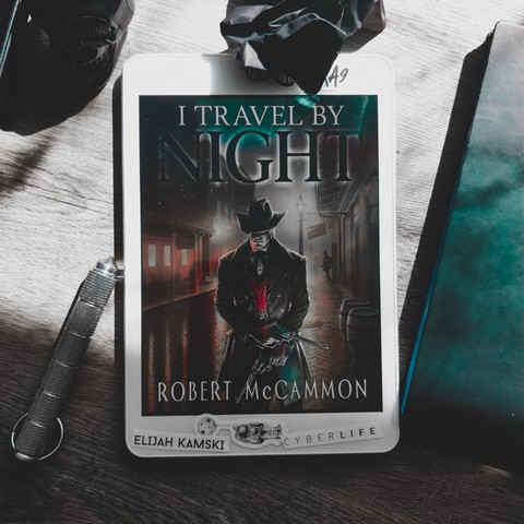 I Travel by Night by Robert McCammon first book in Trevor Lawson book series, a vampire western based in Lousiana during or just after the civil war. Cover depicts a strange looking man with revolvers, wide-brimmed hat covering his eyes, on a well polished street, seemingly wet from the rain, a few lights behind him indicating it's night time. White framed tablet is placed on a greyish dark wooden table, with a few random items around, such as black plastic skull,  a wad of black paper, black notebook, silver colored cilinder with pointy tip, possibly for vampire hunting.