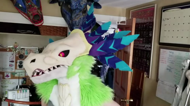 video of a feathered raptor mask with moving jaw. Mask features luminescent eyes, large crest of purple and blue feathers, and a skull-like face.