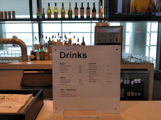 A sign at a United Lounge in Denver International Airport showing a list of complimentary drink options (most are alcoholic).
