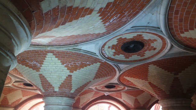 A detail pf the vaulted roof showing the intricate red and white tiling. The black circles are the remains of the gas lights.