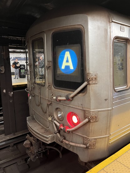 The rear of a subway train displaying a red tail light and a backlit letter A in white inside a blue circle