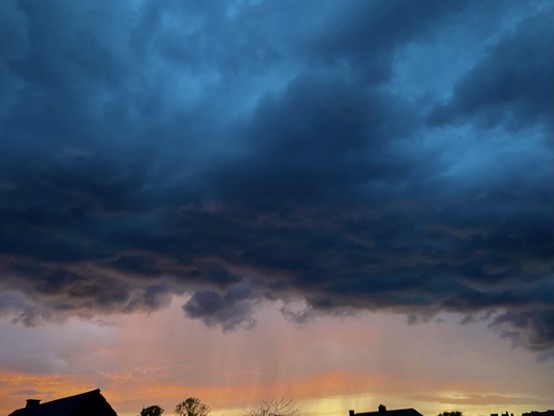 DÃ¼stere Gewitterwolken im Vordergrund, Abendrot und fallender Regen am Horizontâ€¦, am unteren Bildrand sind in knappen Silhouetten gerade eben HausdÃ¤cher zu erkennen.