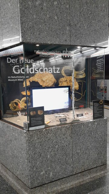 Showcase of the Natural History Museum Vienna at the Volkstheater subway station (U3). The display case contains archaeological tools, information boards, and a screen