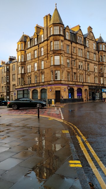 Handsome stone Victorian tenements in the rain, partly reflected in puddles on the nearby pavement