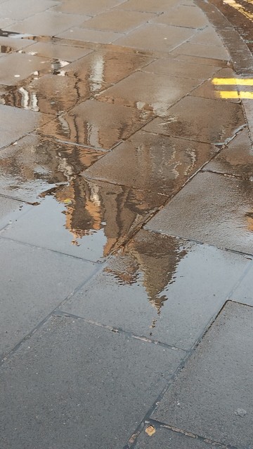 Handsome stone Victorian tenements in the rain, partly reflected in puddles on the nearby pavement
