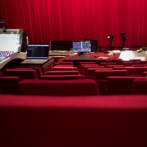 Empty rows of red seats with soundboards, lighting consoles, computers and director’s tables on top, and a closed red curtain in the background. The auditorium of the Staatstheater Darmstadt during an intermission of director Dirk Schmeding’s dress rehearsal of Jacques Offenbach's opera Les Contes d’Hoffmann at the Staatstheater Darmstadt on September 21, 2023.