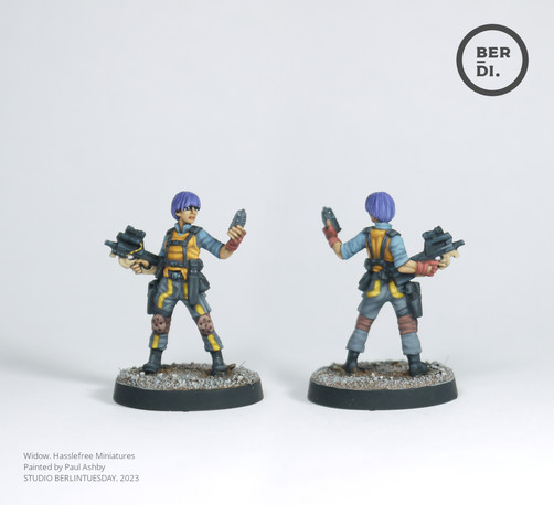 Wargame model. Cyberpunk style. Female gunner with purple hair, orange undershirt, blue-grey trousers with a bright yellow angled line running down them. She stands with a snub-nosed machine gun in one hand and she checks a small computer in the other.