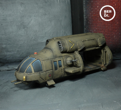 Wargame model. A sizable military transporter. A little like a helecopter, with an open bay to the back for troopers to enter or exit. Its overall an olive drab colour. Well-used, with scuffs and dirt.