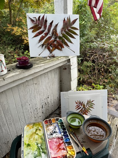 Photo: view of where I'm painting on the porch with model leaves on railing taped to white board. Below the in-progress photo peeks out behind low surface holding paint palette, brushes and water.