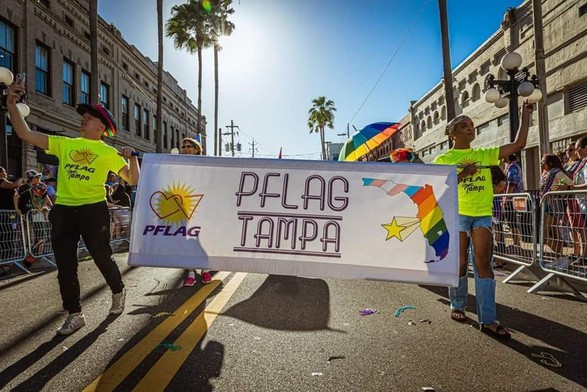 PFLAG Tampa parade banner being held by two members in the Tampa Pride parade. The banner is backlit by the bright Florida sun.