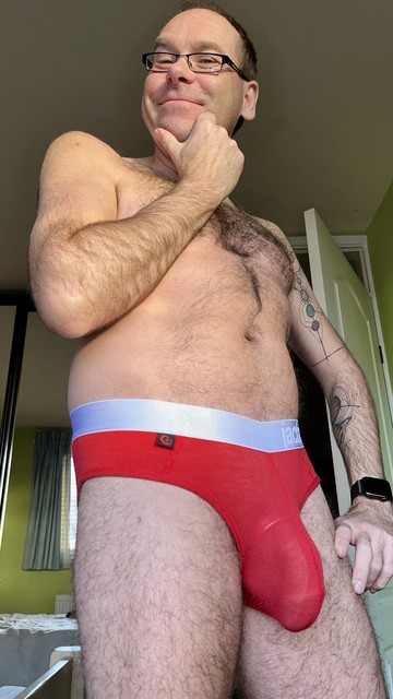 Hairy gay guy wearing read Jack Adams Naked Fit briefs, his cock and balls held in a cockring and bulging visibly through the thin material